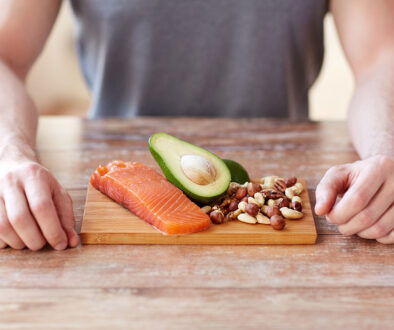 Closeup Of Fish, Avocado, & Nuts On A Cutting Board In Front Of A Man Foods To Prevent Colon Cancer